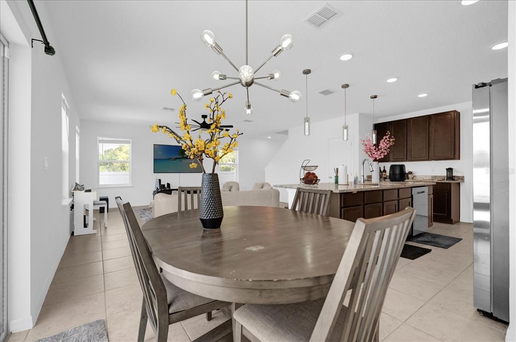 A dining area with a round wooden table sits in front of an open kitchen — 4432 DESERT ROSE AVENUE, KISSIMMEE, FL