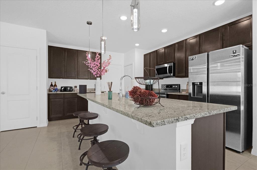 A kitchen features dark wood cabinets, granite countertops, a central island, and stainless steel appliances — 4432 DESERT ROSE AVENUE, KISSIMMEE, FL