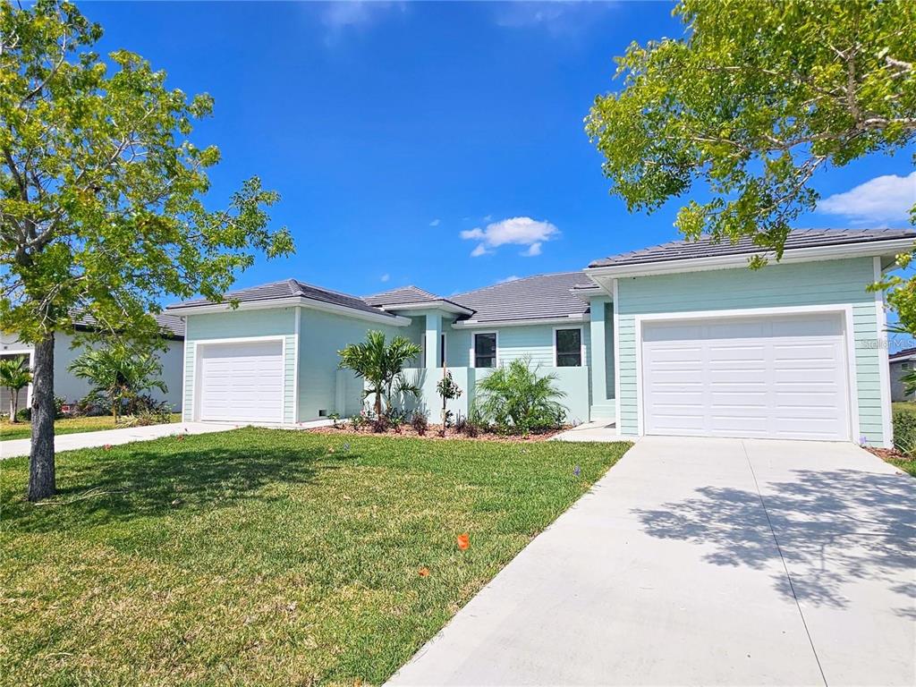 A light green single-story house features two white garage doors and a concrete driveway — 174 MADRID BOULEVARD, PUNTA GORDA, FL