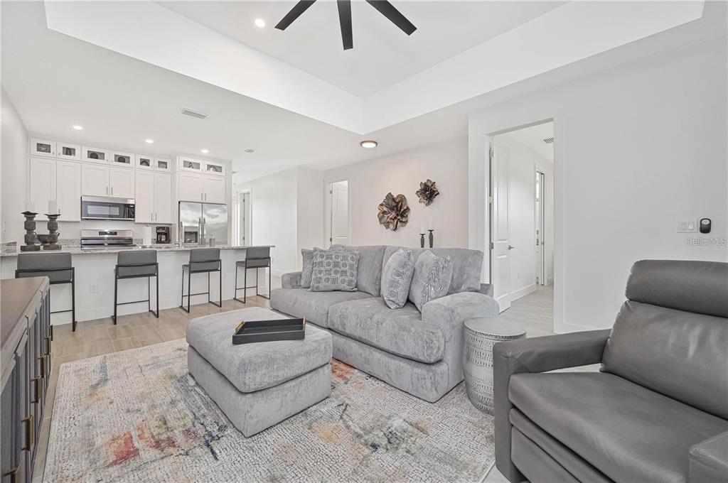 A modern open-concept living room features a gray sofa, kitchen island, and white cabinetry — 174 MADRID BOULEVARD, PUNTA GORDA, FL