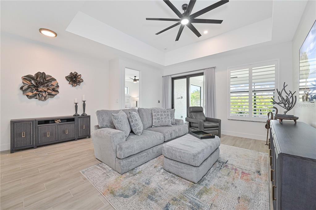 A living room features a gray sofa, matching ottoman, ceiling fan, and light wood flooring — 174 MADRID BOULEVARD, PUNTA GORDA, FL