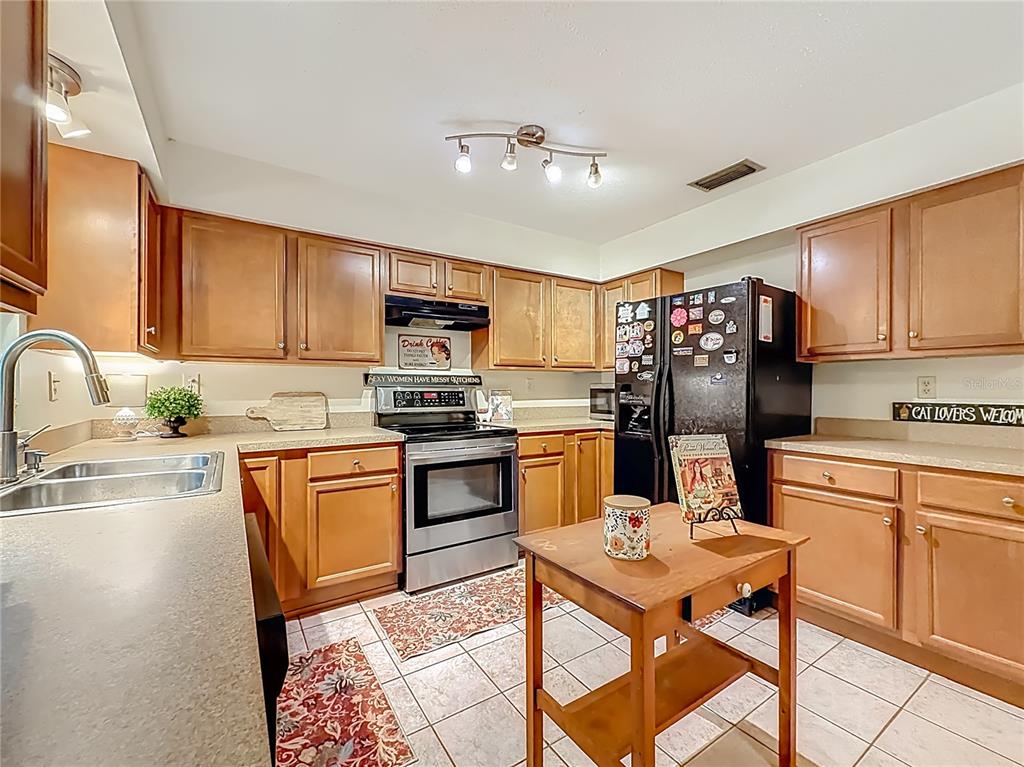 A kitchen features wood cabinets, stainless steel appliances, a small island, and tiled flooring — 3301 SE 34TH STREET, OCALA, FL