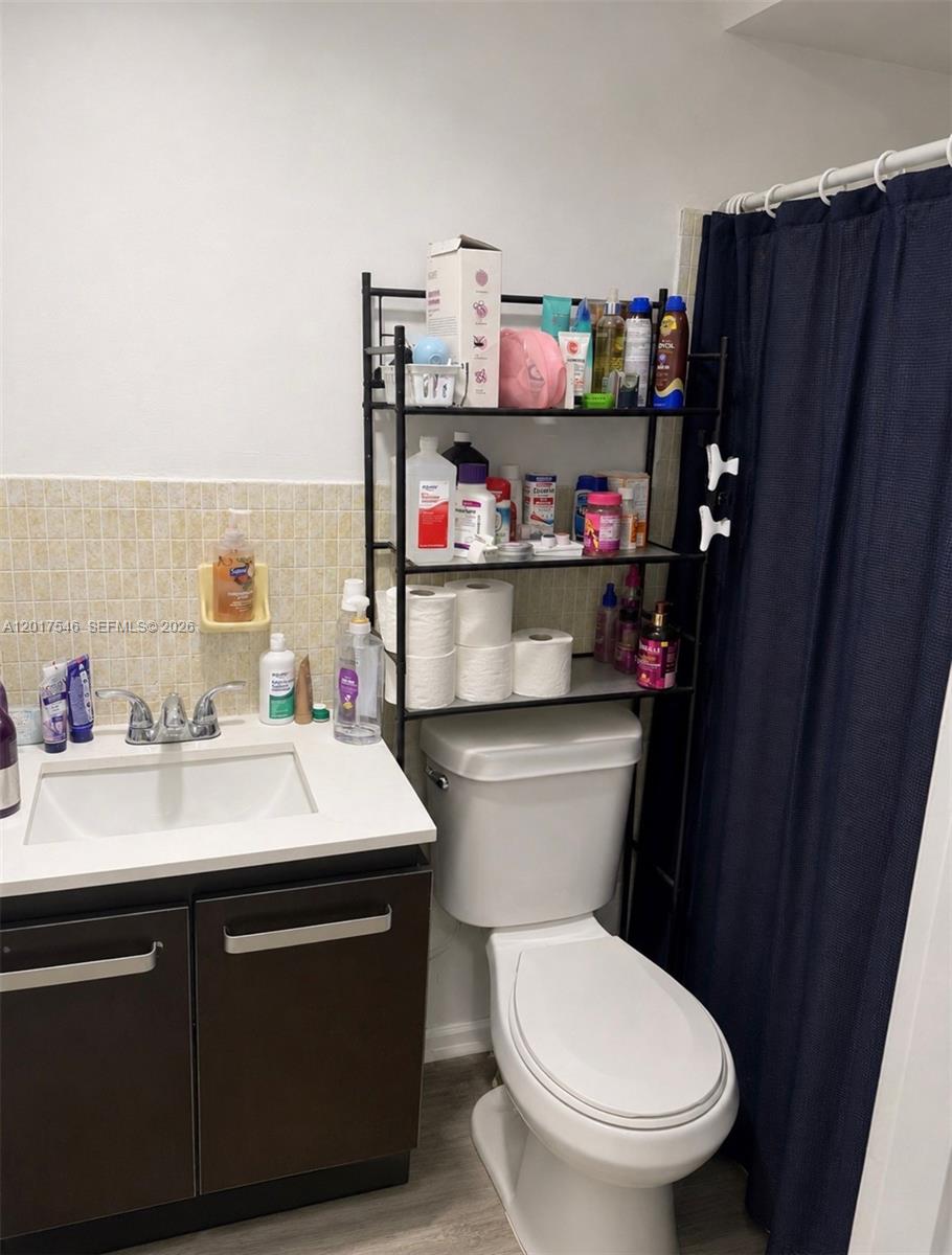 A bathroom features a vanity with a white countertop, a toilet, and a metal shelving unit — 685 Miller Dr # E205, Miami Springs FL 33166, MIAMI SPRINGS, FL