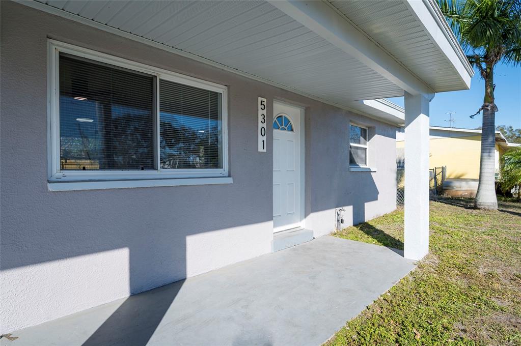 A gray house exterior features a concrete porch, a white front door, and a large window — 5301 97TH TERRACE N, PINELLAS PARK, FL