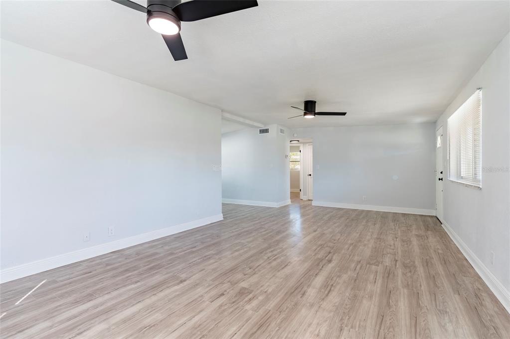 An empty room with light wood-look flooring, white walls, and two black ceiling fans — 5301 97TH TERRACE N, PINELLAS PARK, FL