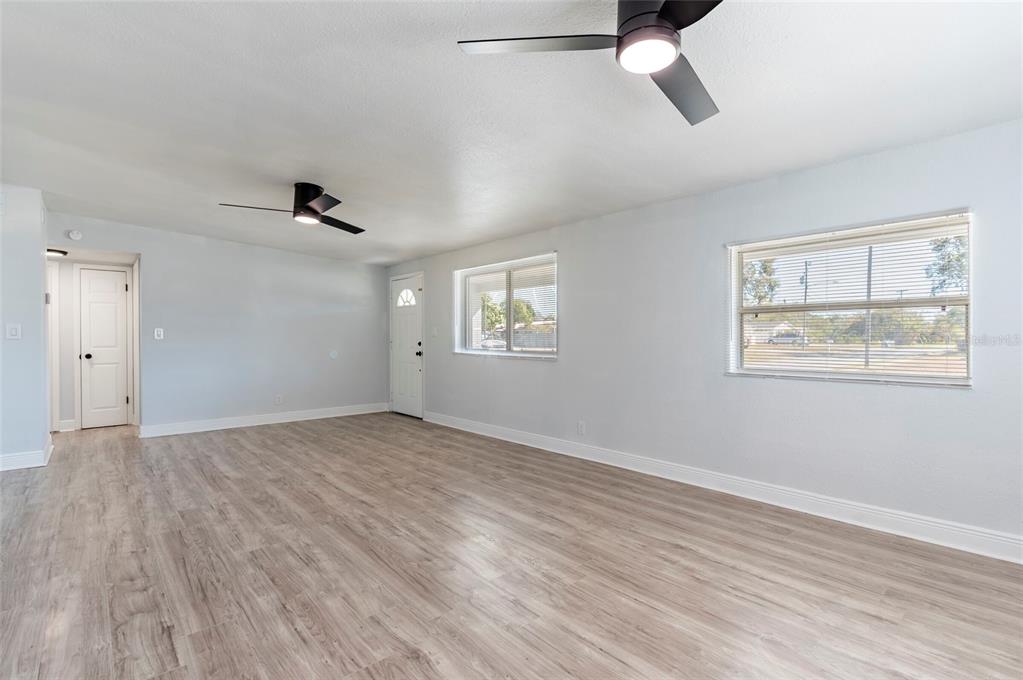 An empty living room features light wood-look flooring, two ceiling fans, and two windows — 5301 97TH TERRACE N, PINELLAS PARK, FL