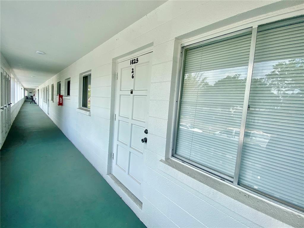 An exterior walkway of a multi-story building features white doors and windows with blinds — 1825 FLAMINGO BOULEVARD UNIT O26, BRADENTON, FL