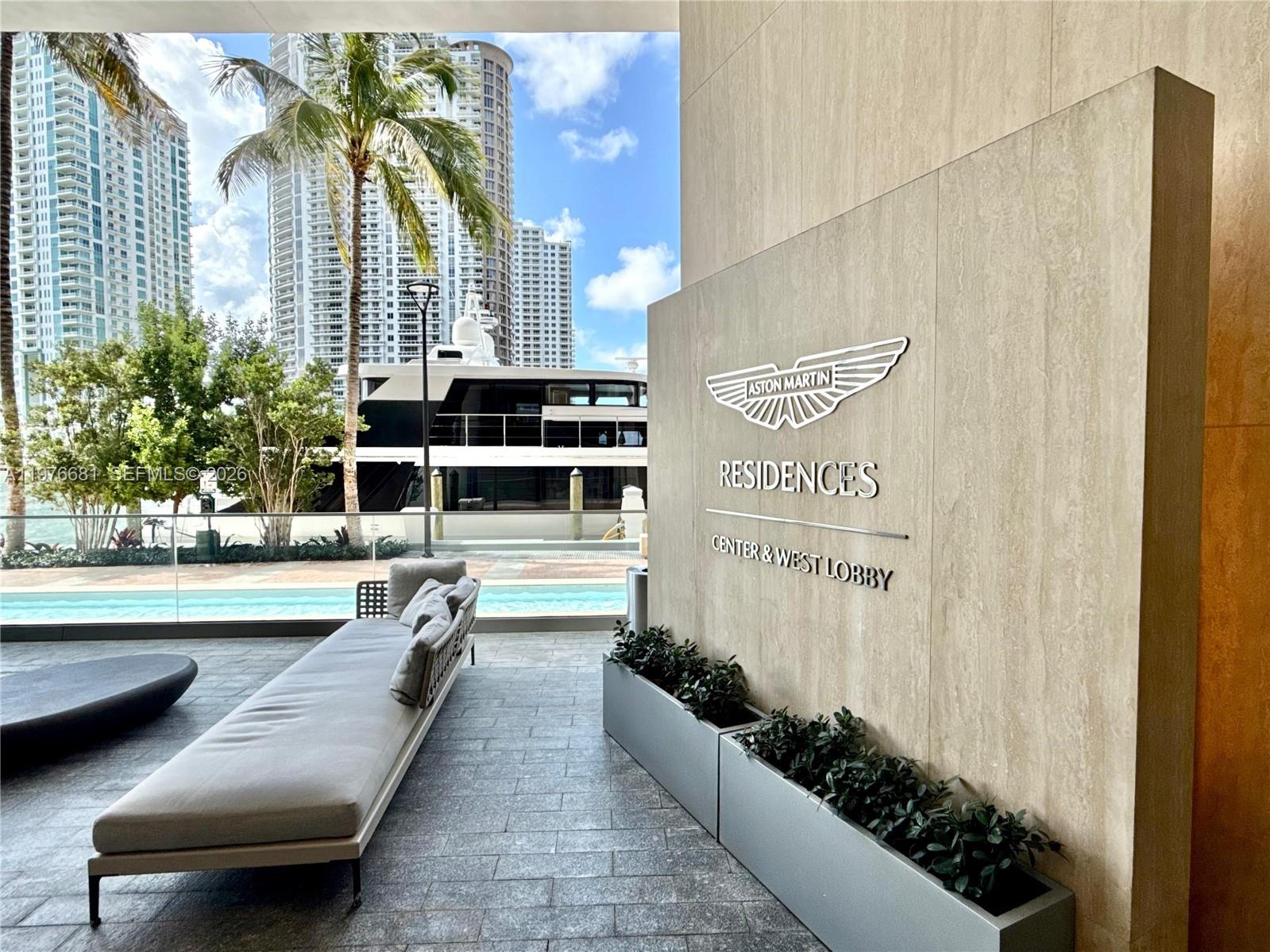 A modern outdoor lounge area features a long sofa, planters, and an Aston Martin sign — 300 Biscayne Boulevard Way # 3608W, Miami FL 33131, MIAMI, FL