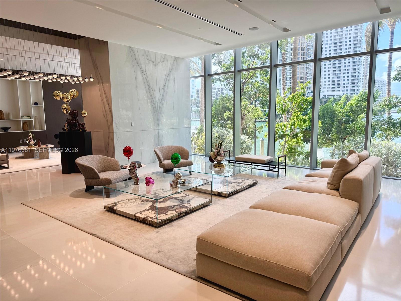 A modern living room features marble walls, glass coffee tables, and floor-to-ceiling windows overlooking water — 300 Biscayne Boulevard Way # 3608W, Miami FL 33131, MIAMI, FL