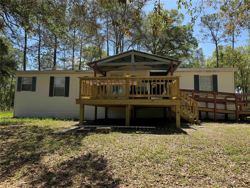 A mobile home exterior features a wooden deck with a covered porch and a ramp — 1550 SE 111TH COURT, MORRISTON, FL