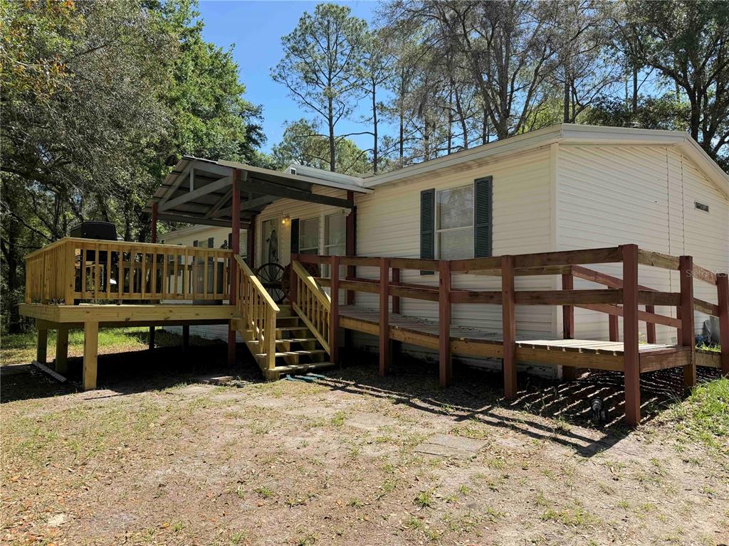 A mobile home exterior features a wooden deck, a wheelchair ramp, and a covered porch — 1550 SE 111TH COURT, MORRISTON, FL