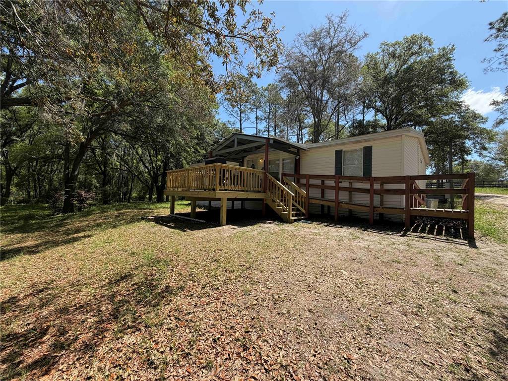 A mobile home exterior features a wooden deck and a ramp leading to the entrance — 1550 SE 111TH COURT, MORRISTON, FL