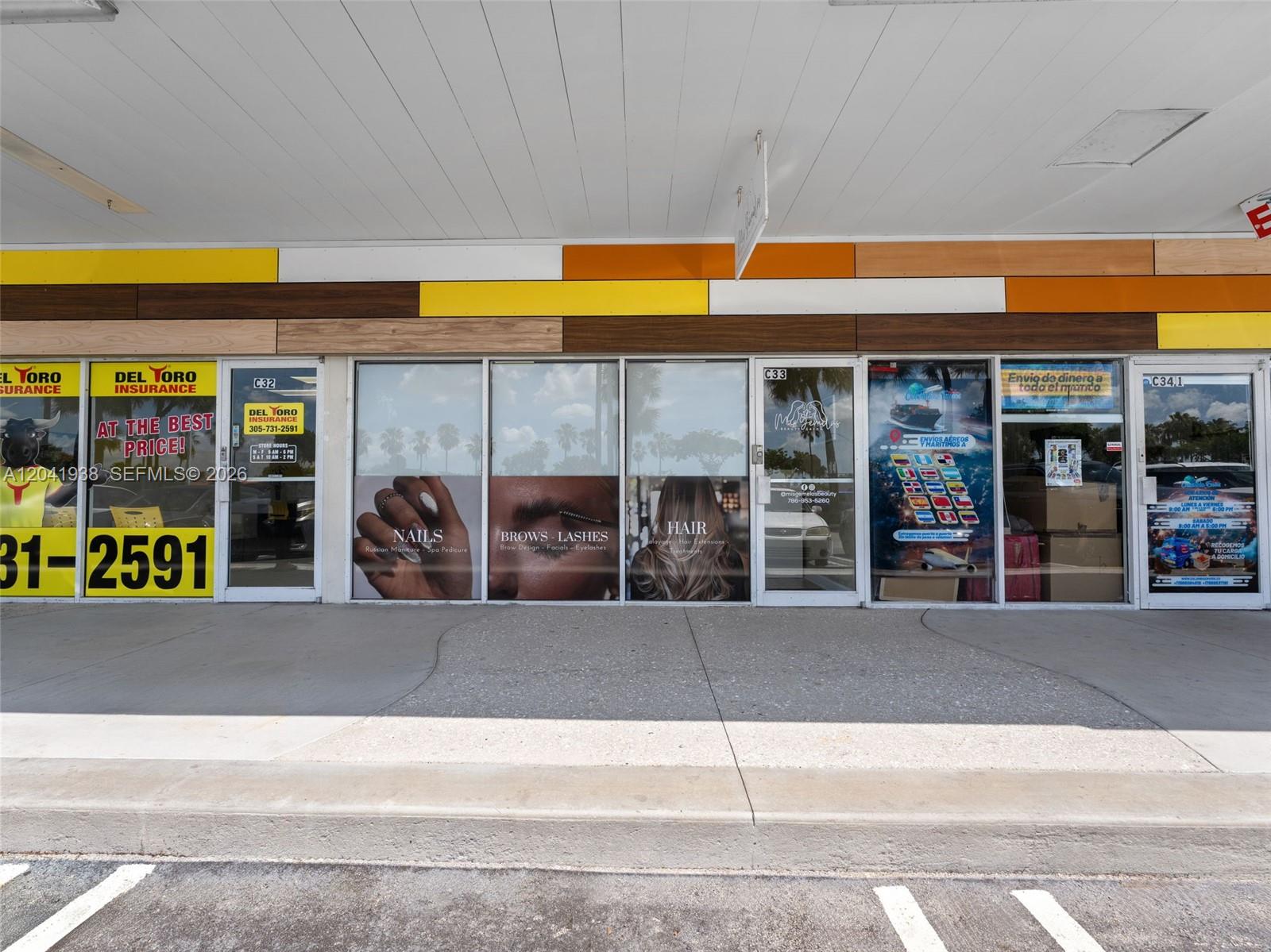 The exterior of a commercial strip mall storefront features glass windows with beauty salon signage — MIAMI, FL