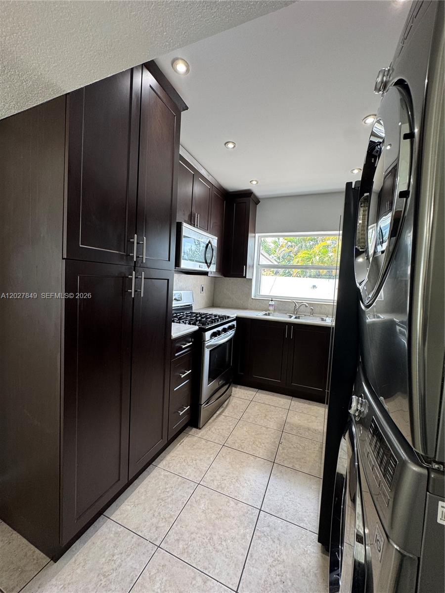 A galley kitchen features dark wood cabinets, stainless steel appliances, and light-colored tile flooring — 7420 Big Cypress Dr, Miami Lakes FL 33014, MIAMI LAKES, FL