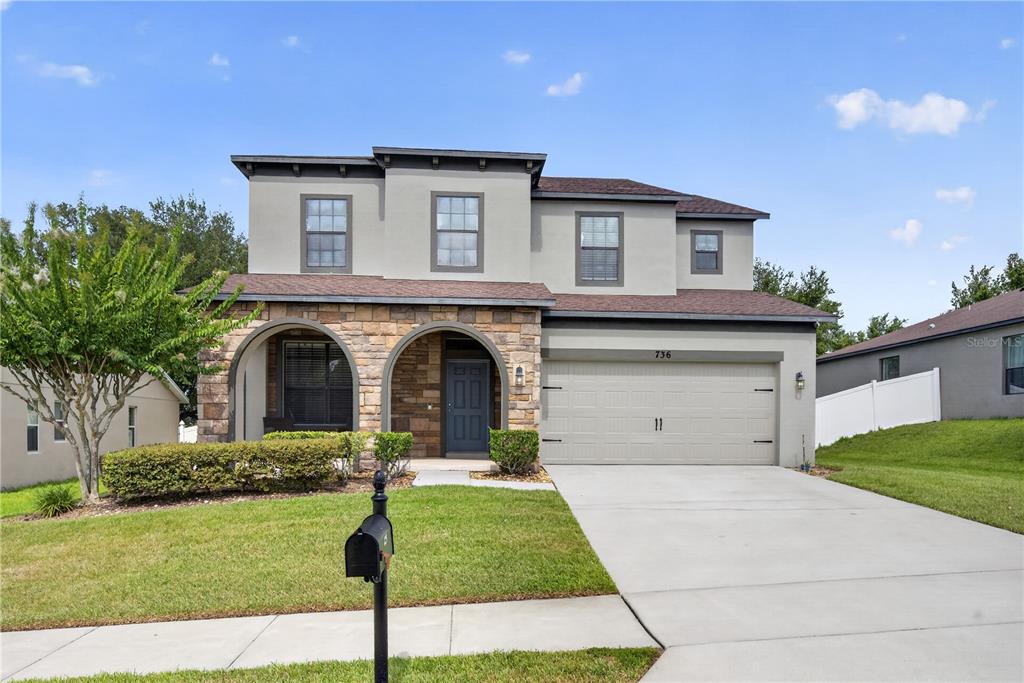 A two-story house with a stone facade, arched entryway, and an attached two-car garage — 736 WOODS LANDING DRIVE, MINNEOLA, FL