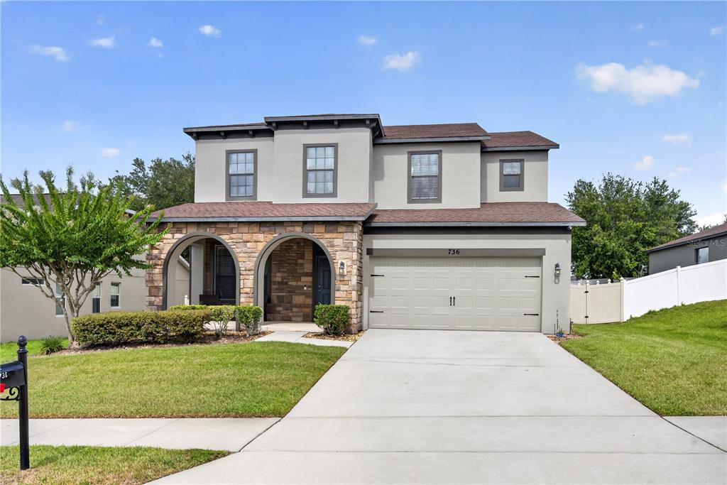 A two-story house with a stone-accented facade, arched entryway, and a two-car garage — 736 WOODS LANDING DRIVE, MINNEOLA, FL