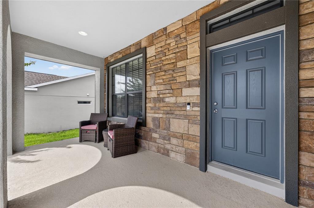 A covered porch features a blue front door, stone veneer siding, and two wicker chairs — 736 WOODS LANDING DRIVE, MINNEOLA, FL