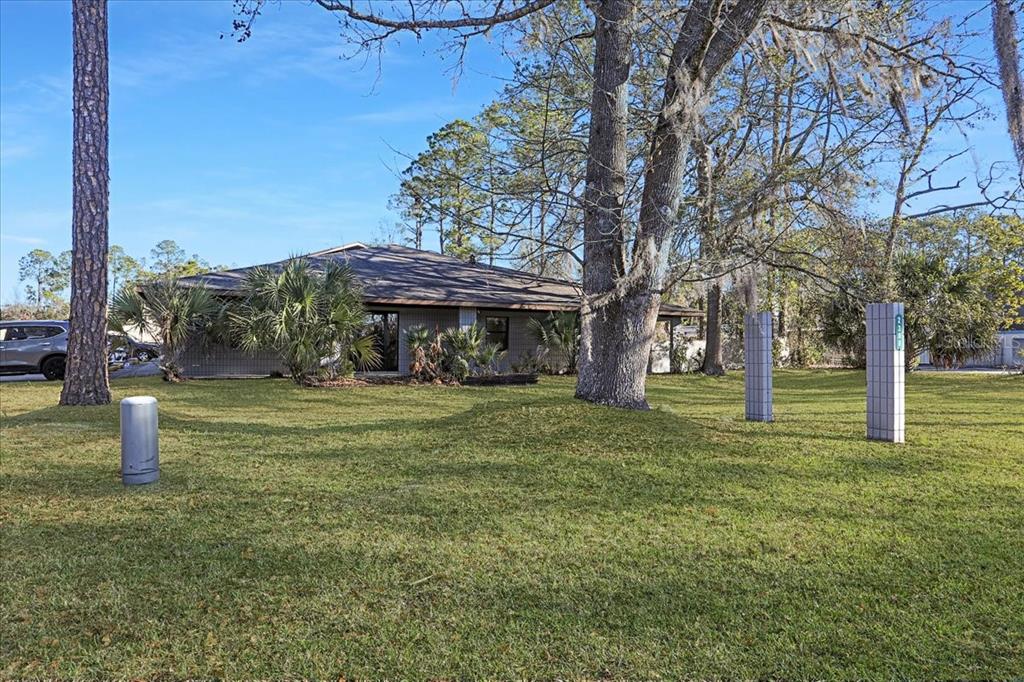 A single-story house with a gray exterior sits on a grassy lot with large trees — 2300 NW 71ST PLACE, GAINESVILLE, FL