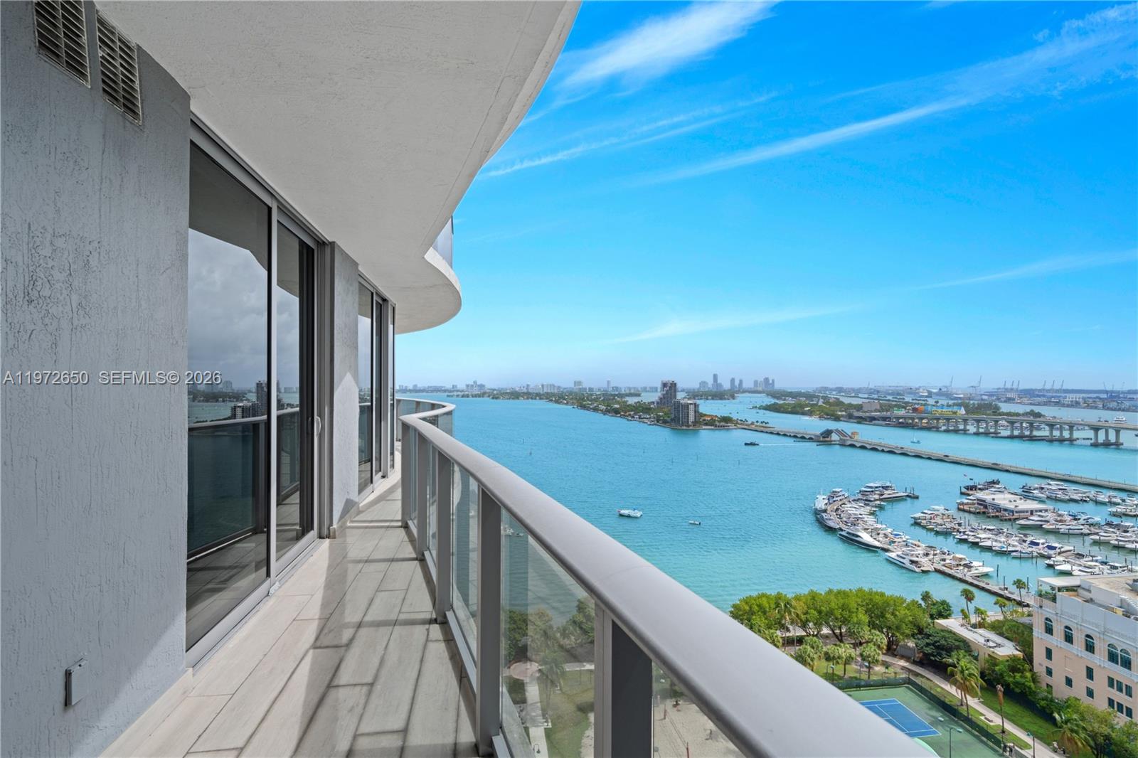 A curved balcony with glass railings overlooks a bay, a marina, and a bridge — 488 NE 18th St # 2112, Miami FL 33132, MIAMI, FL