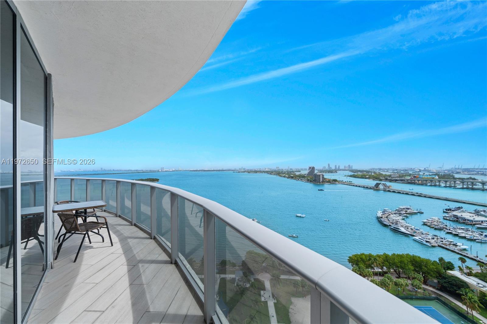 A high-rise balcony with outdoor seating overlooks a bay, a marina, and a bridge — 488 NE 18th St # 2112, Miami FL 33132, MIAMI, FL
