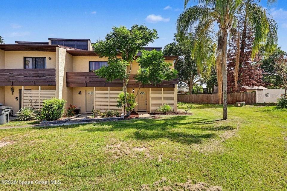 A two-story townhouse exterior with a wooden balcony, slatted privacy screens, and a palm tree — 3156 FINSTERWALD DRIVE, TITUSVILLE, FL