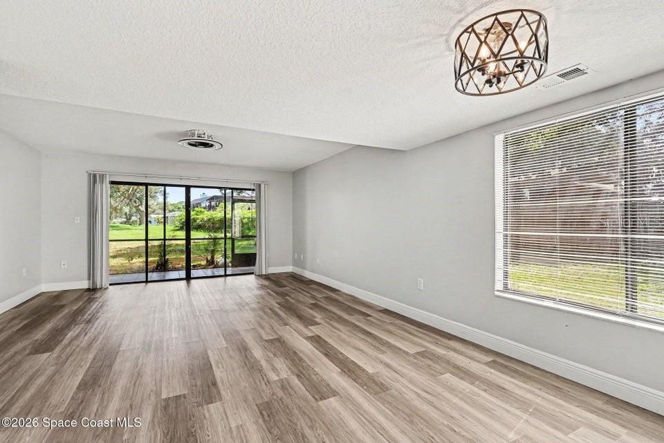A bright living room features light wood-look flooring, a modern light fixture, and sliding glass doors — 3156 FINSTERWALD DRIVE, TITUSVILLE, FL