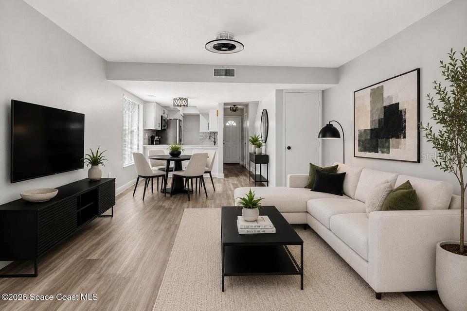 A living room with light wood floors, a white sectional sofa, and an adjacent dining area — 3156 FINSTERWALD DRIVE, TITUSVILLE, FL