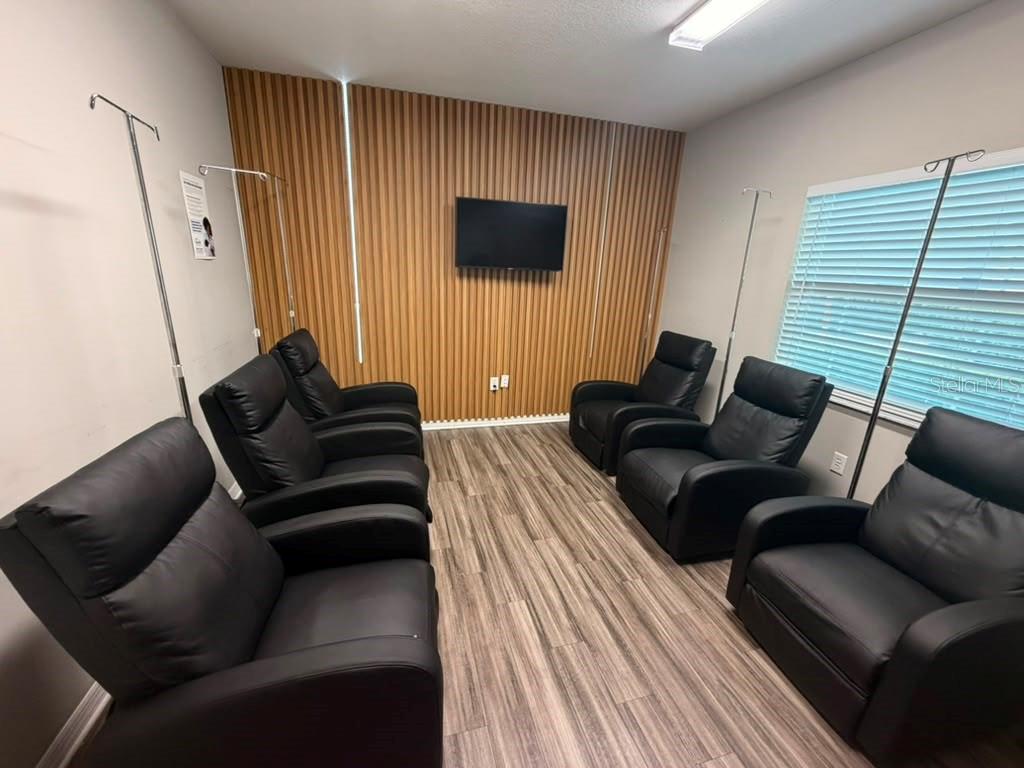 A room with wood-slat wall paneling, wood-look flooring, and several black recliners with IV poles — 3200 HILLSDALE LANE, KISSIMMEE, FL