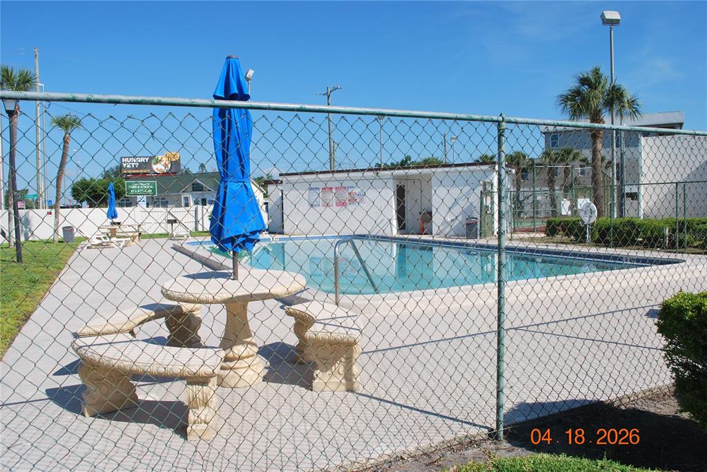 A fenced outdoor swimming pool area features a stone table with benches and an umbrella — 9201 TUDOR DRIVE UNIT C215, TAMPA, FL