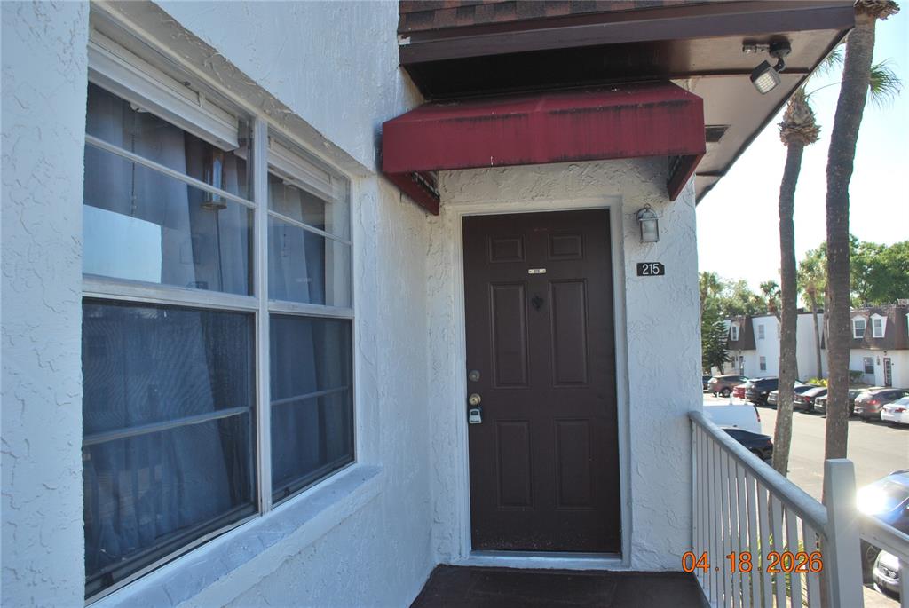 A brown front door with a red awning is situated on a white building exterior — 9201 TUDOR DRIVE UNIT C215, TAMPA, FL