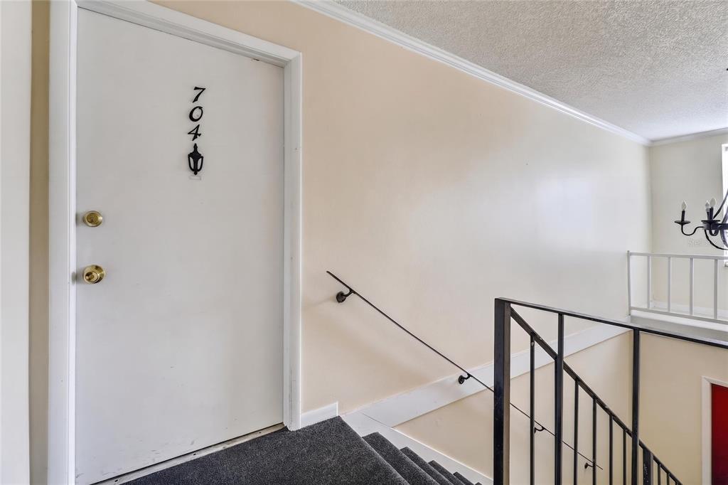 A white door labeled 704 stands at the top of a carpeted staircase — 200 SAINT ANDREWS BOULEVARD UNIT 704, WINTER PARK, FL