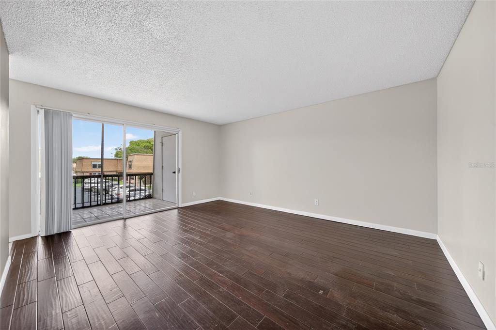 An empty room with dark wood-look flooring, light walls, and a sliding glass balcony door — 200 SAINT ANDREWS BOULEVARD UNIT 704, WINTER PARK, FL