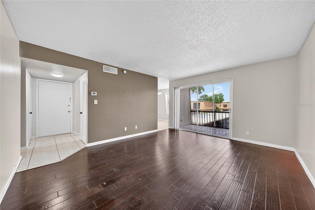 An empty living room features dark wood flooring, a brown accent wall, and sliding glass doors — 200 SAINT ANDREWS BOULEVARD UNIT 704, WINTER PARK, FL