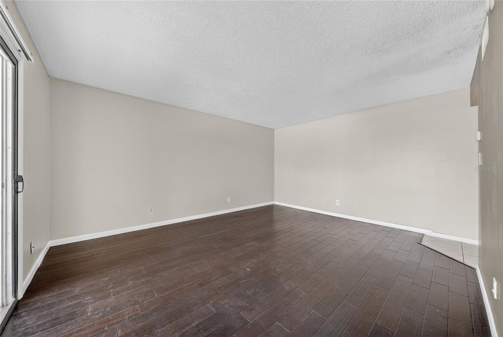 An empty room with dark wood-look flooring, light-colored walls, and a sliding glass door — 200 SAINT ANDREWS BOULEVARD UNIT 704, WINTER PARK, FL