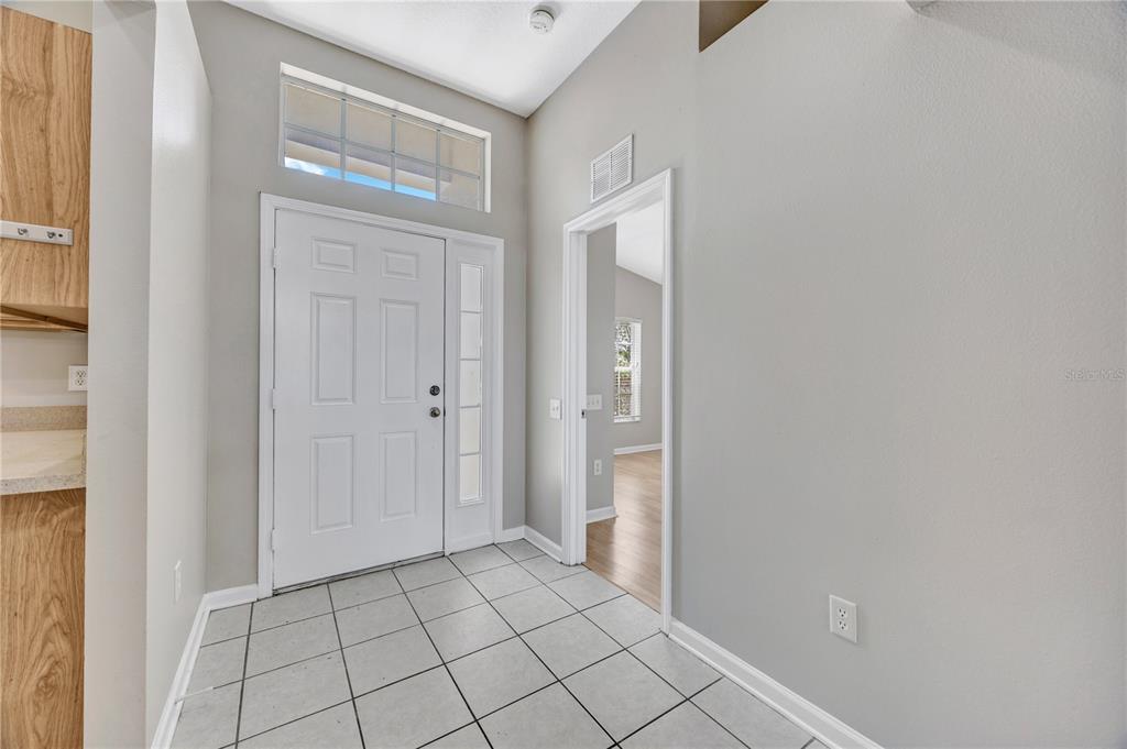 An entryway with white tiled floors, a front door with a sidelight, and gray walls — 30435 ANNADALE DRIVE, WESLEY CHAPEL, FL