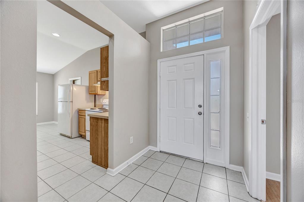 An entryway with tiled floors leads to a kitchen featuring wood cabinets and white appliances — 30435 ANNADALE DRIVE, WESLEY CHAPEL, FL