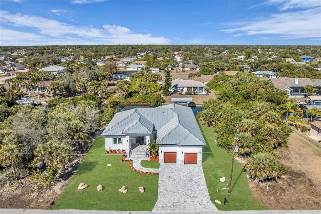 A modern white house with a metal roof and two wooden garage doors — 18702 ARAPAHOE CIRCLE, PORT CHARLOTTE, FL