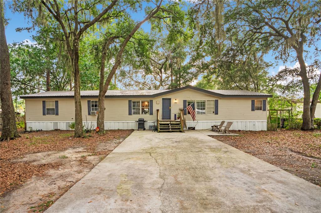 A single-story manufactured home with beige siding, a concrete driveway, and surrounding mature oak trees — 2322 STATE PARK ROAD, LAKELAND, FL