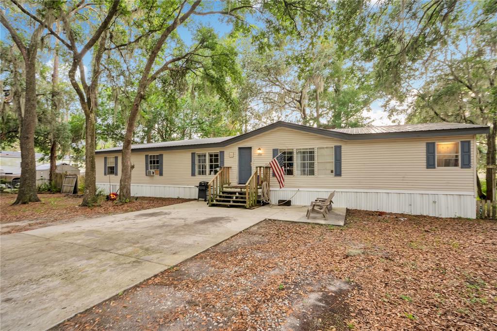 A single-story manufactured home with beige siding, dark shutters, and a front wooden porch — 2322 STATE PARK ROAD, LAKELAND, FL