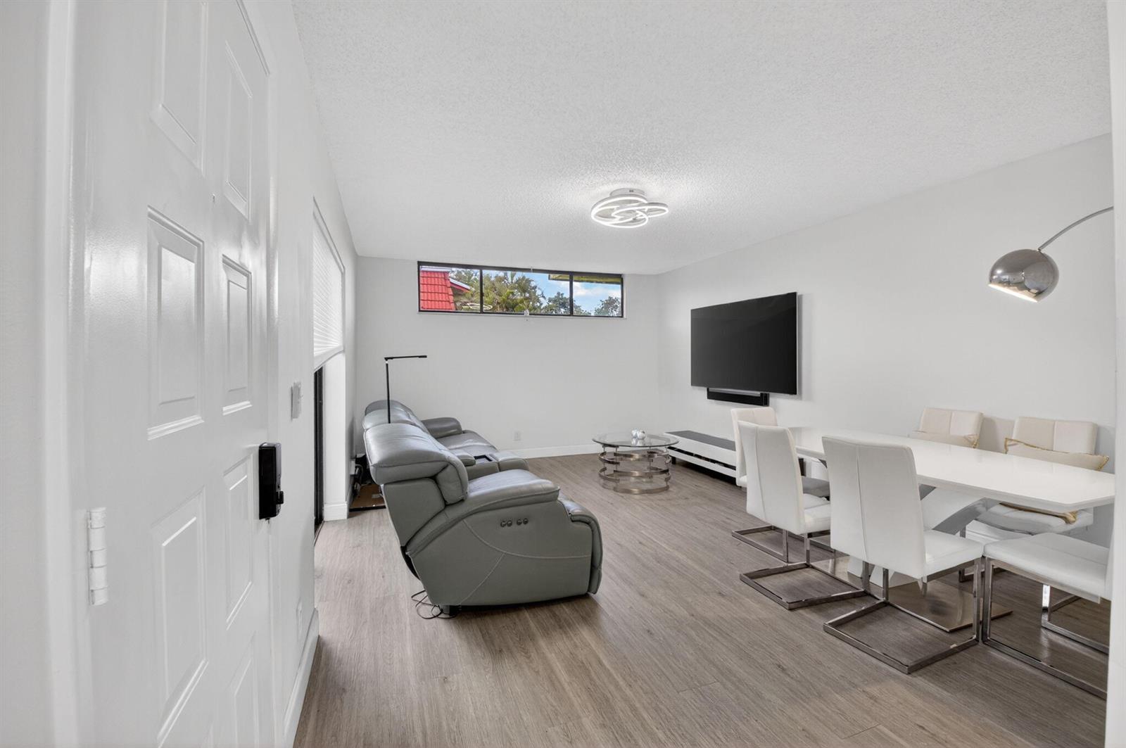 A living and dining area features gray flooring, white walls, a sectional sofa, and a television — 8385 Trent Court # D, Boca Raton FL 33433, BOCA RATON, FL