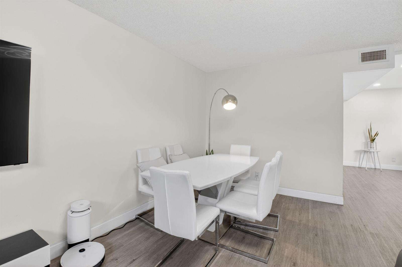 A dining area features a white table, four white chairs, and a modern floor lamp — 8385 Trent Court # D, Boca Raton FL 33433, BOCA RATON, FL
