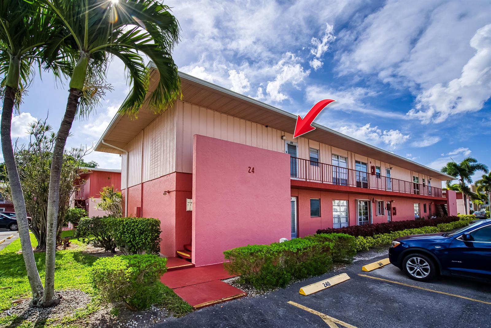 The exterior of a pink two-story apartment building features a red arrow pointing to a unit — 24 Golfs Edge # D, West Palm Beach FL 33417, WEST PALM BEACH, FL