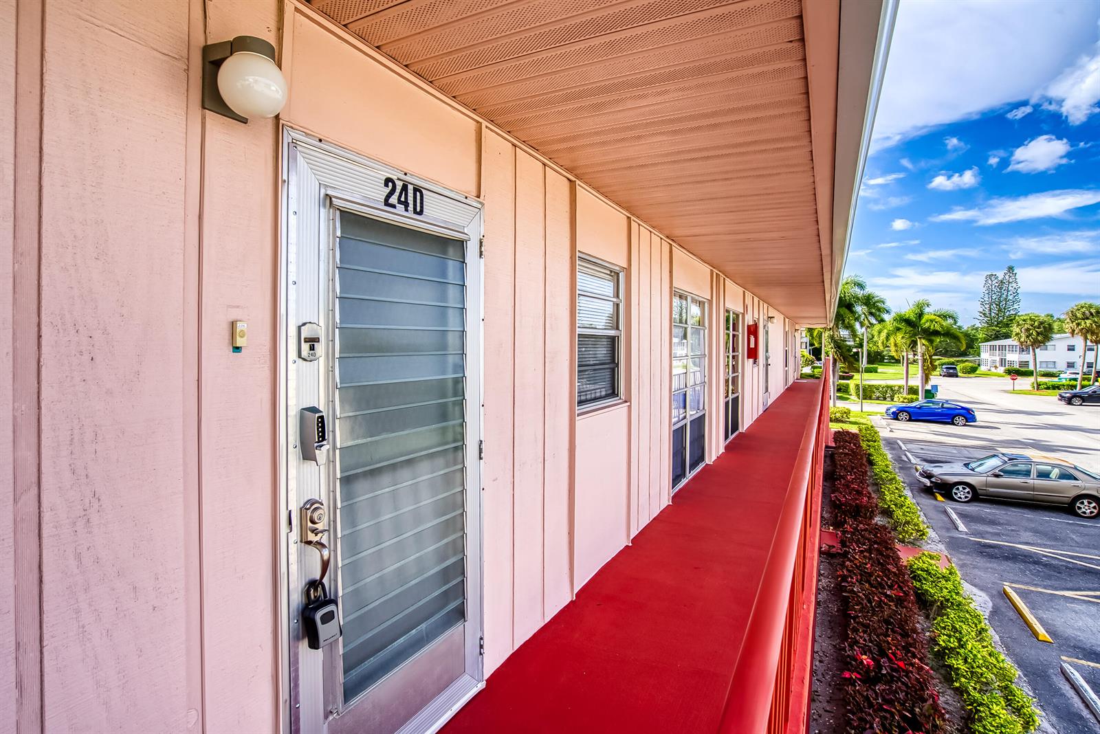 An exterior walkway with a red floor leads past a pink building with numbered doors — 24 Golfs Edge # D, West Palm Beach FL 33417, WEST PALM BEACH, FL