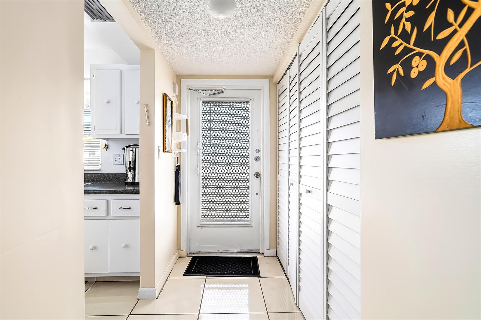 A tiled entryway features a white door, louvered closet doors, and a view into a kitchen — 24 Golfs Edge # D, West Palm Beach FL 33417, WEST PALM BEACH, FL