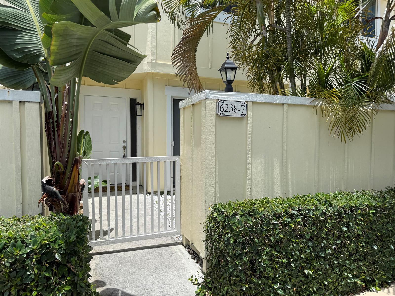 A white gate leads to the entrance of a yellow home with a house number sign — 6238 Riverwalk Lane # 7, Jupiter FL 33458, JUPITER, FL