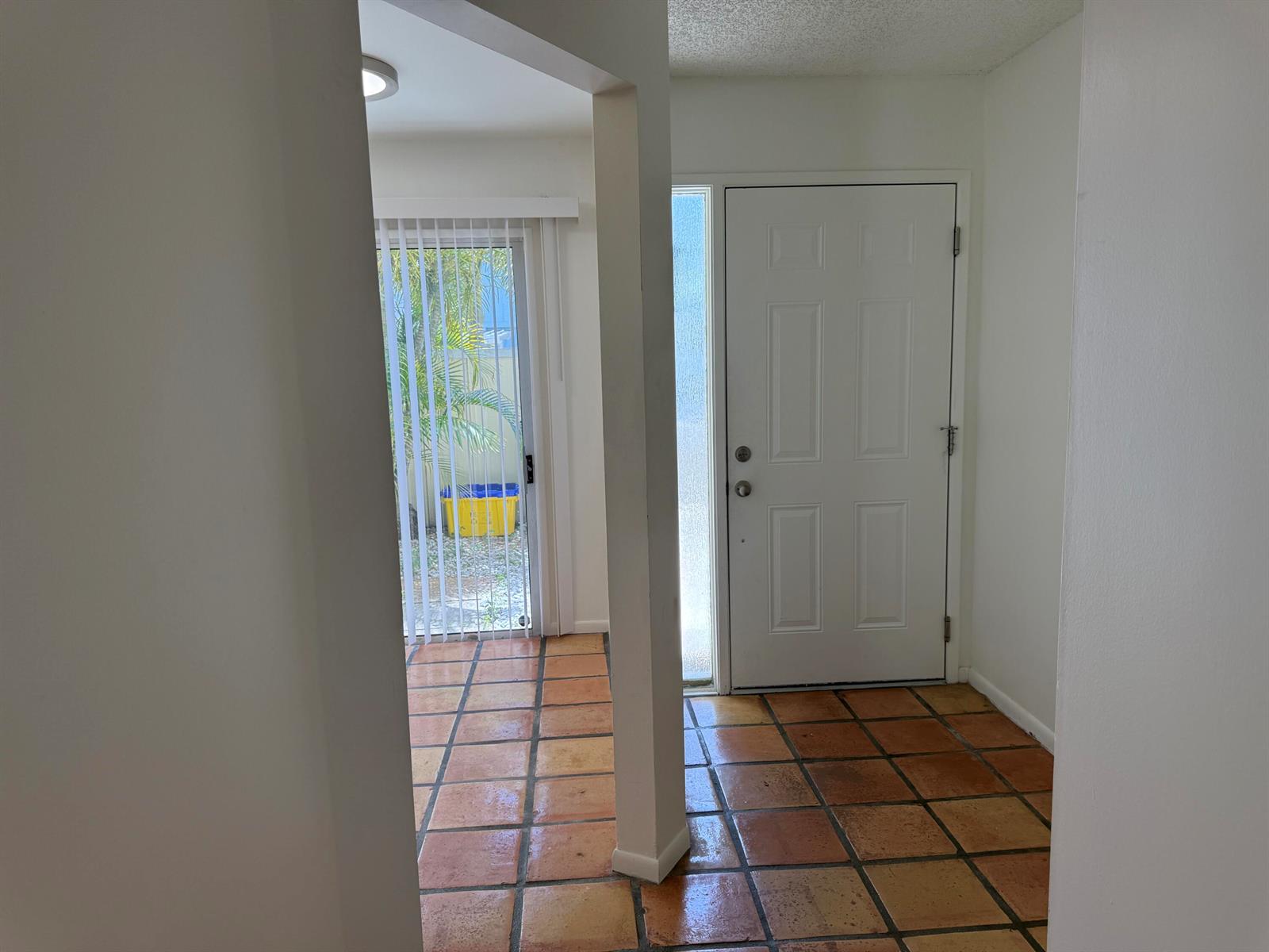 An entryway with terracotta tile flooring leads to a white front door and sliding glass door — 6238 Riverwalk Lane # 7, Jupiter FL 33458, JUPITER, FL