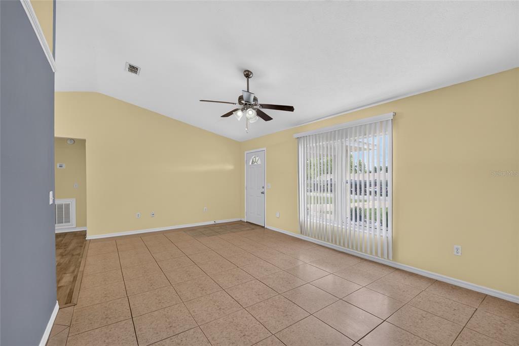 A living room with light yellow walls, tile flooring, a ceiling fan, and vertical blinds — 16 FIR TRAIL COURSE, OCALA, FL