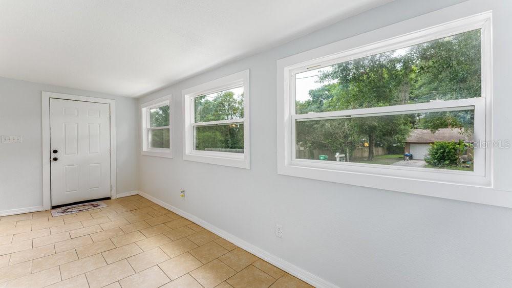 A bright room with light gray walls, tile flooring, a white door, and large windows — 912 E CAROLINA AVE, DELAND, FL