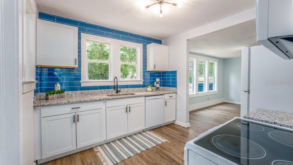 A kitchen with white cabinets, granite countertops, blue subway tile backsplash, and wood-look flooring — 912 E CAROLINA AVE, DELAND, FL