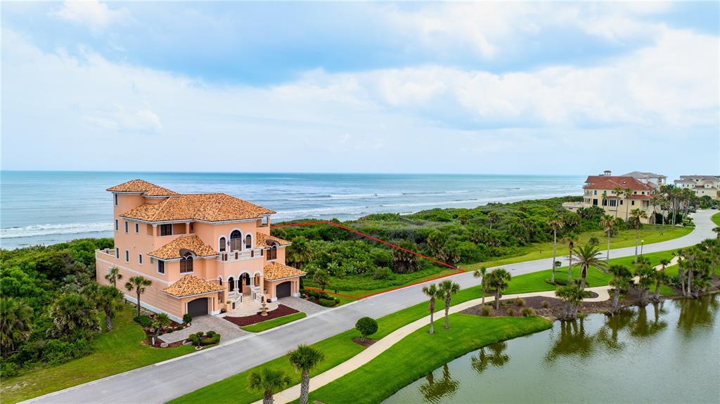 An aerial view shows a large peach-colored house next to a vacant, outlined oceanfront lot — 73 CALLE DEL SUR Lot 50, PALM COAST, FL